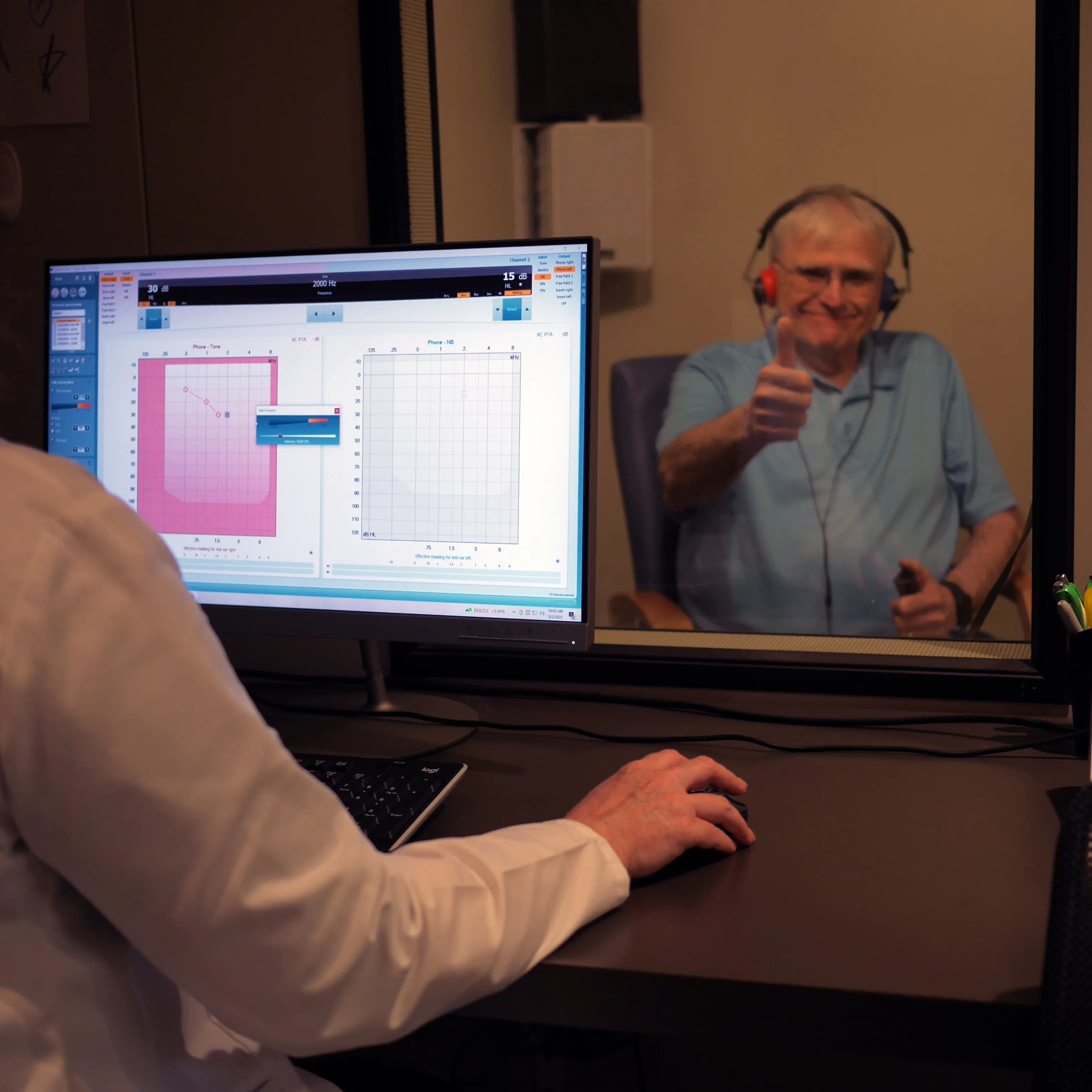 A patient gives a thumbs up from the sound booth during a hearing test at Hearing Specialty Center
