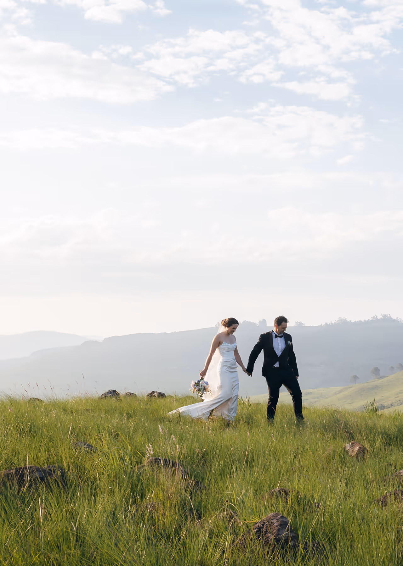 Backyard garden with green grass, a tree, a brick wall, and a black metal table surrounded by five matching chairs.