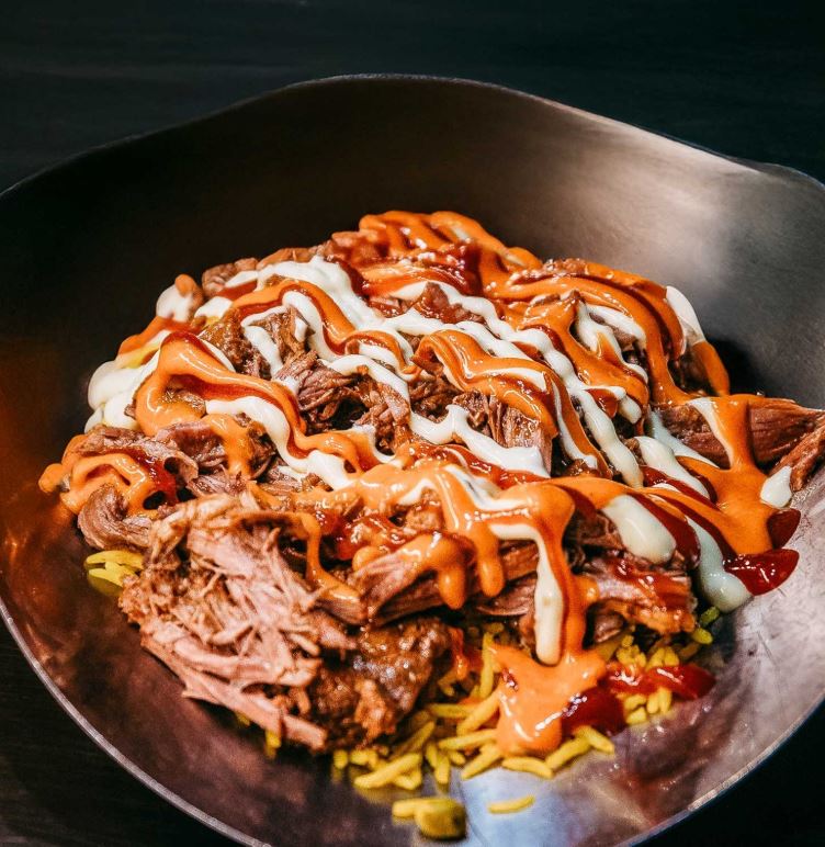 Loaded rice topped with savoury meat, fresh garnishes, and a mix of flavorful sauces