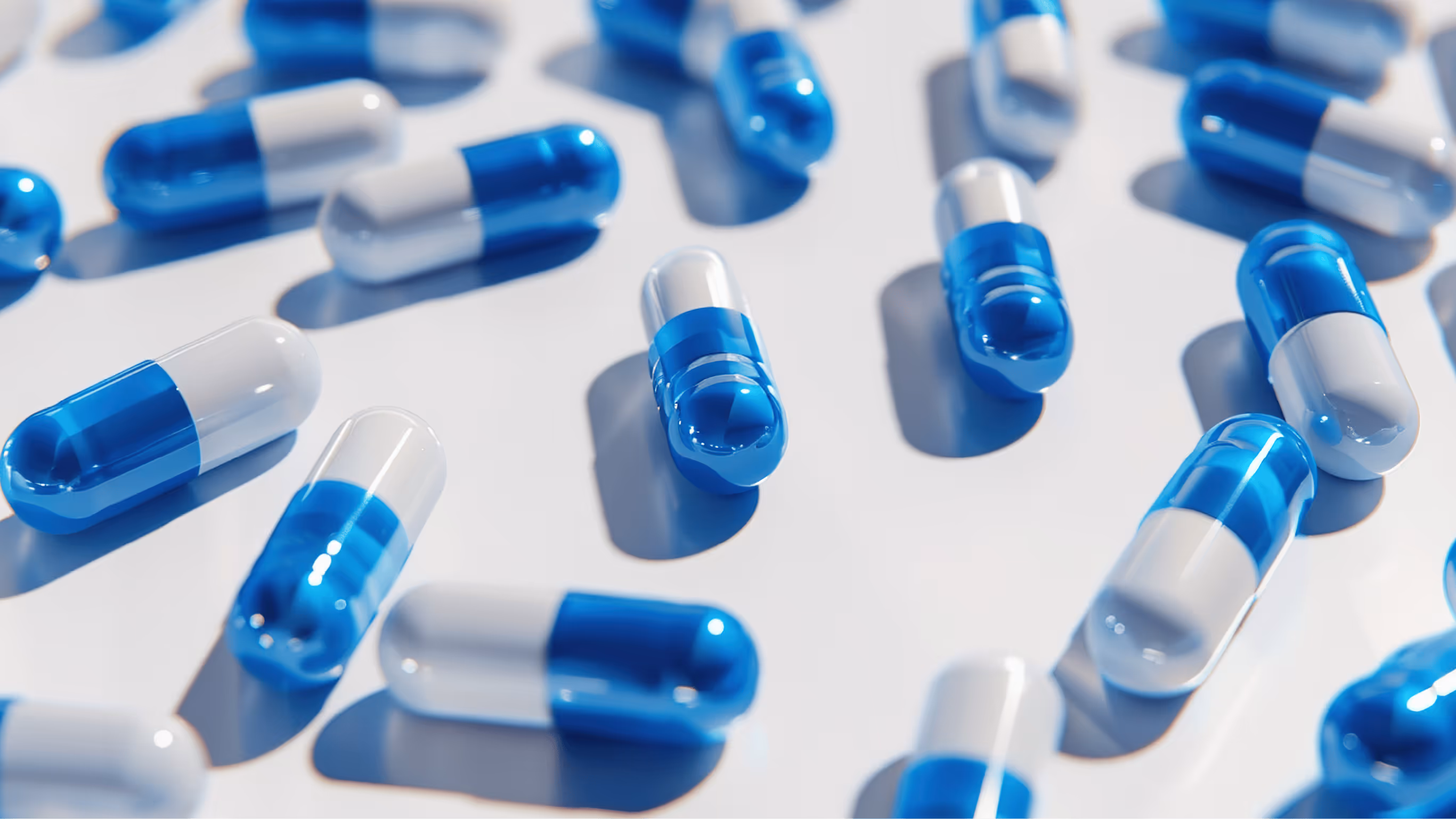 Blue and white pharmaceutical capsules scattered on a white background