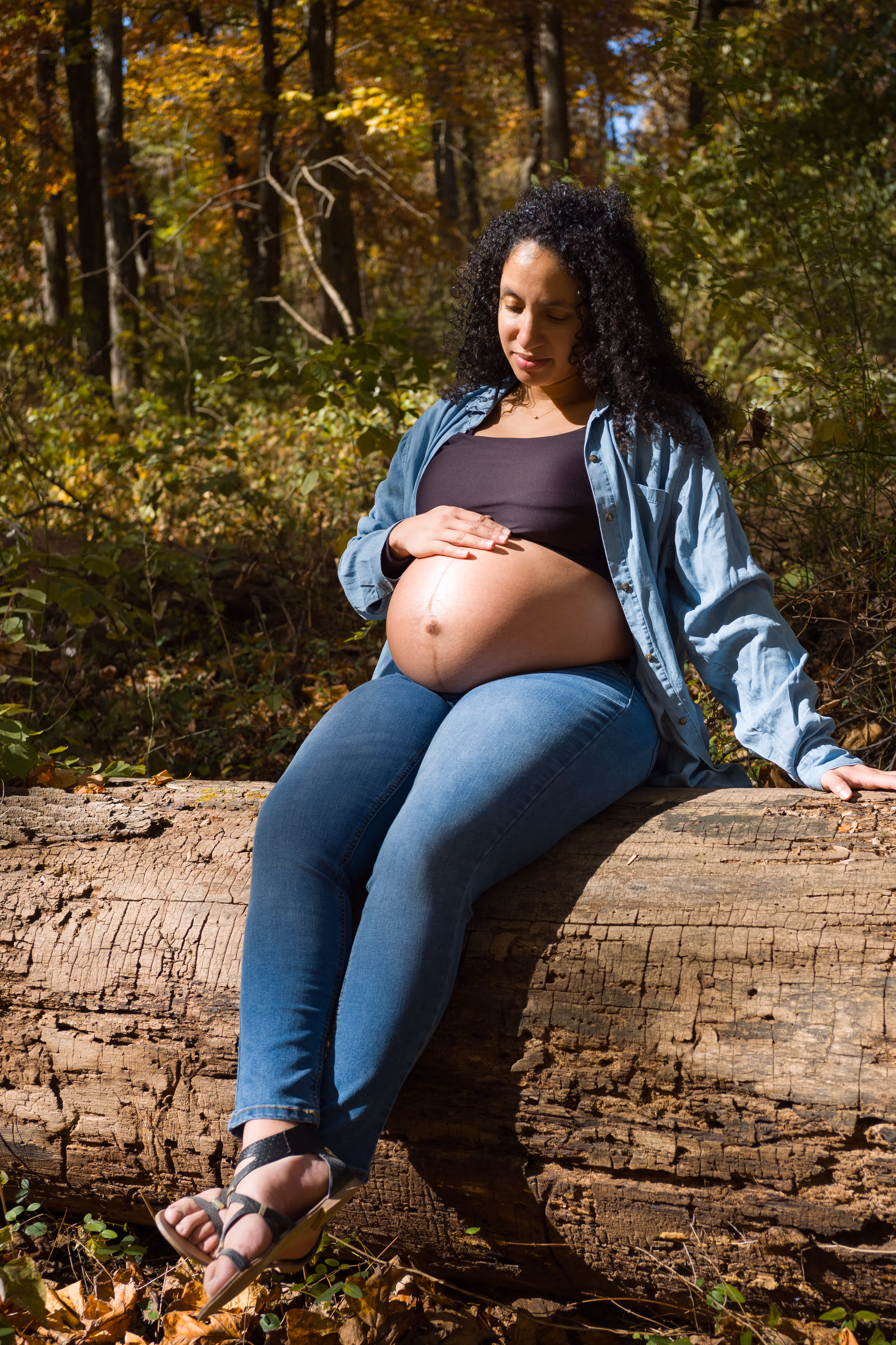 A woman sitting on a log with her belly showing.