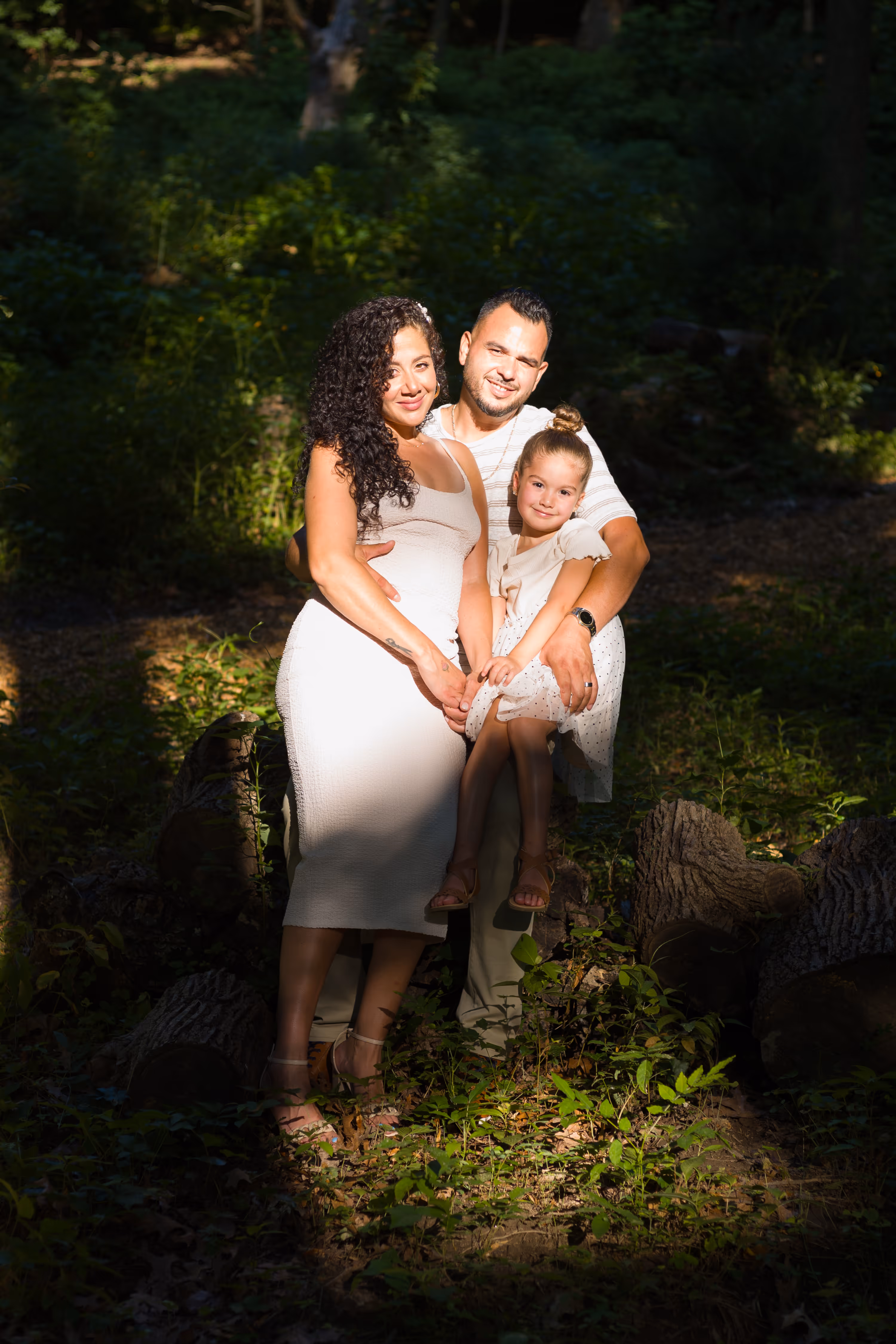A woman, a man, and a child pose for a picture in a forest.