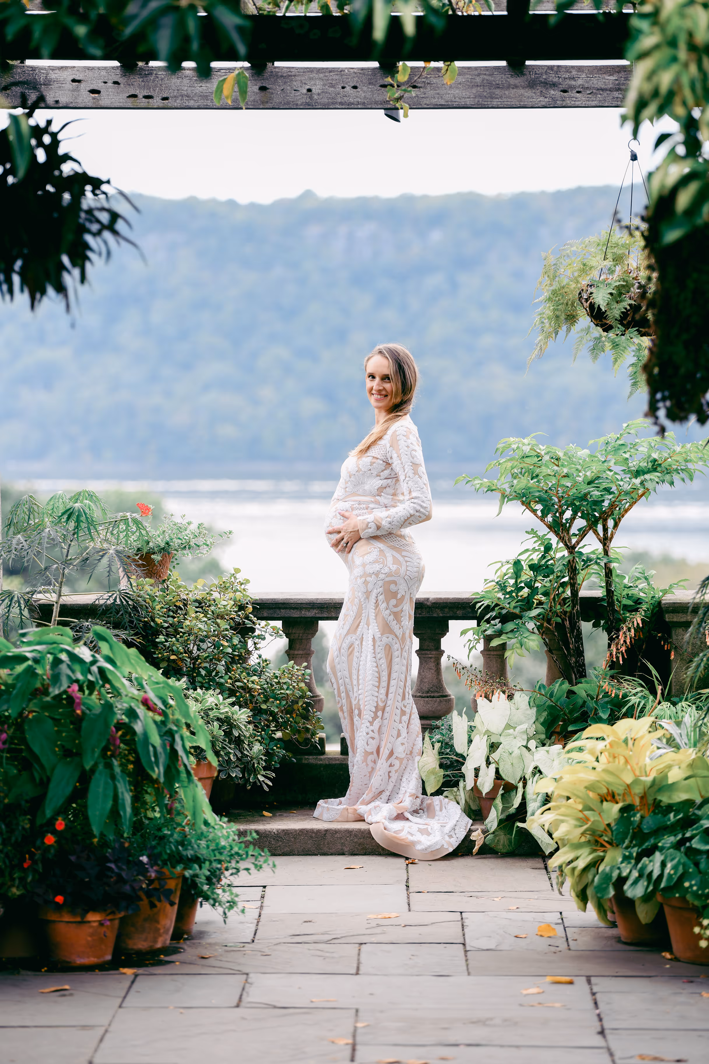 A woman in a white dress stands on a patio with a view of the water.
