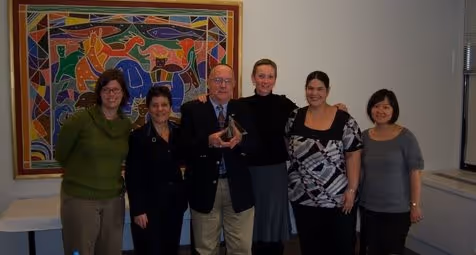 Three women smiling and holding glass awards under a red Story Brook Cancer Center banner.
