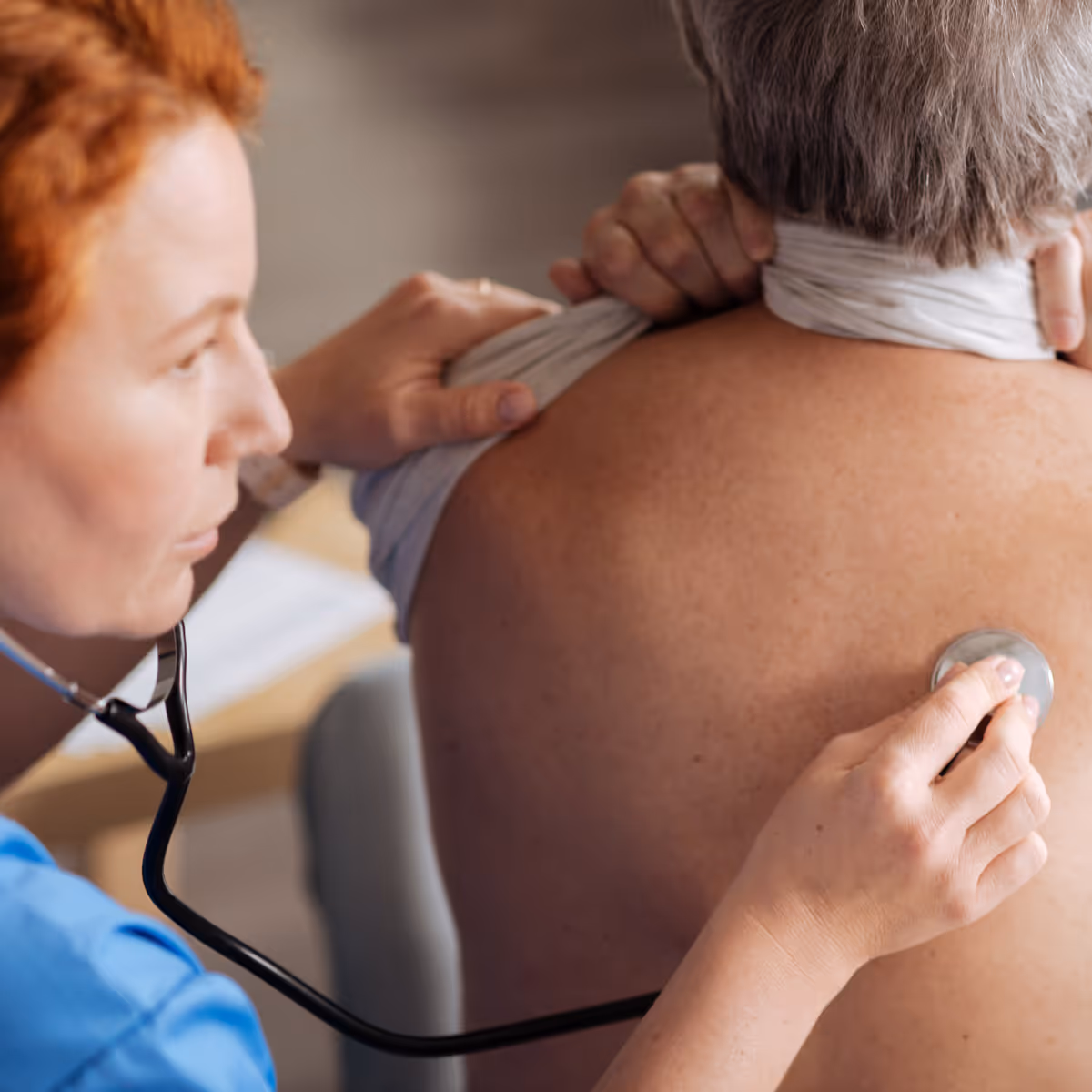 Healthcare professional using a stethoscope to listen to an elderly patient's back.