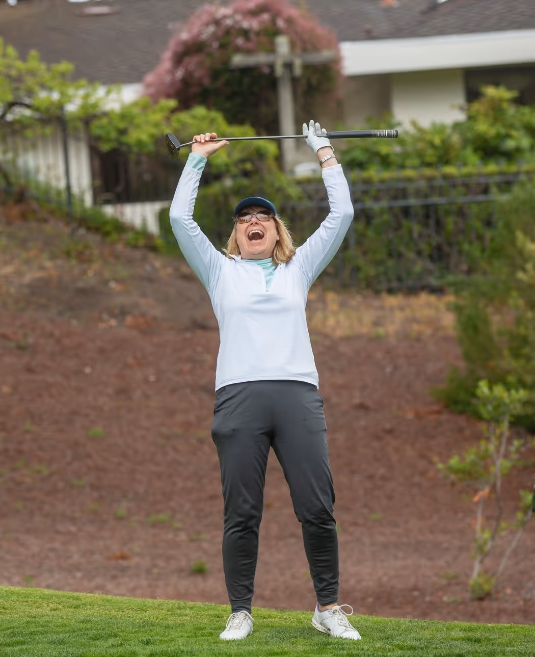 Woman in golf attire raising a putter above her head in celebration on a golf course.