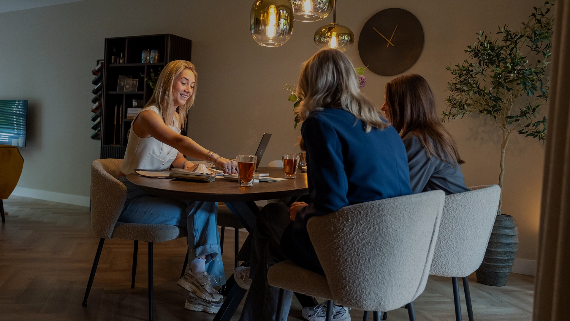 Interieurontwerpster Anouk geeft advies aan twee klanten aan een ronde tafel in een sfeervol ingerichte ruimte met warme verlichting.