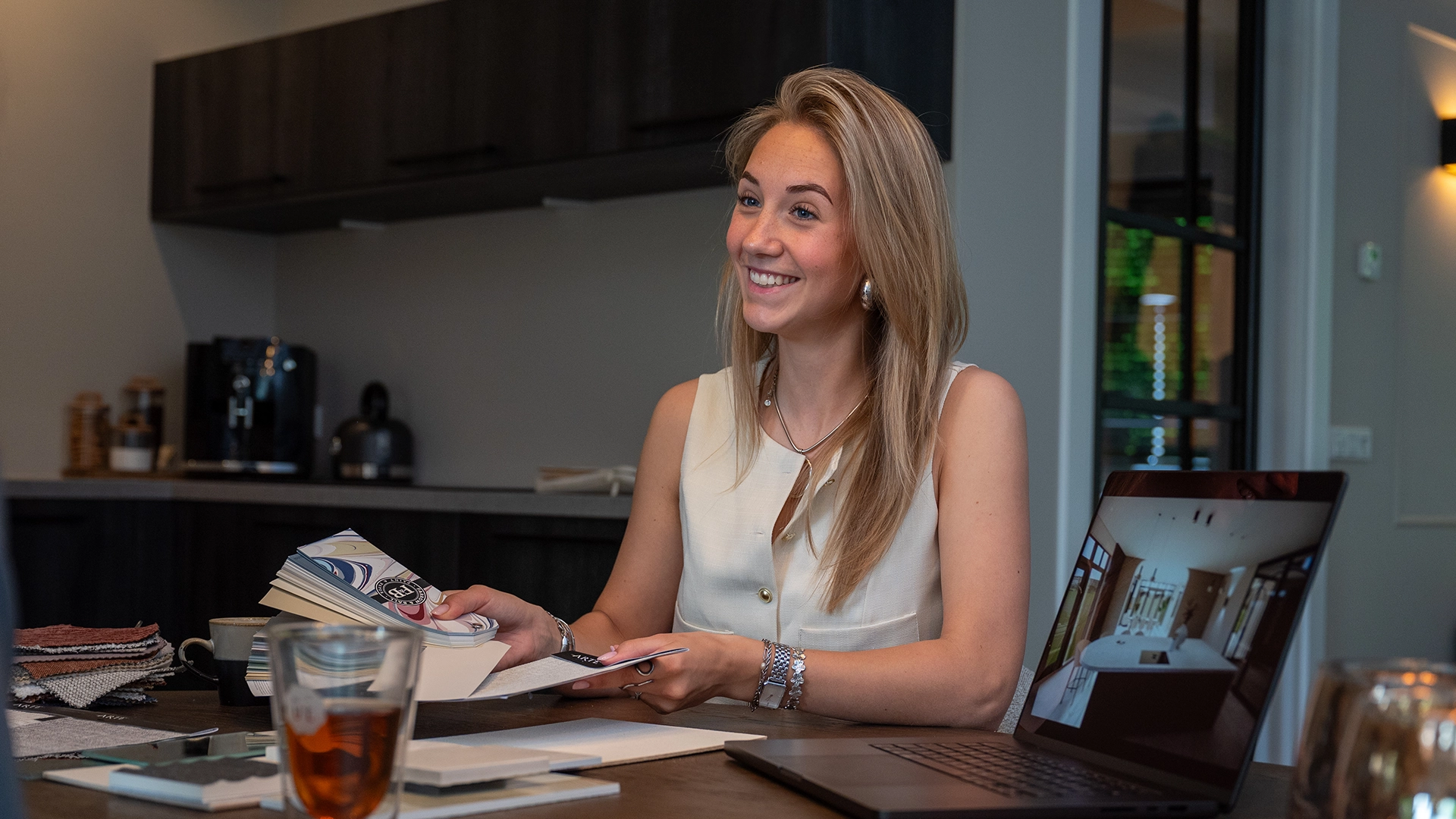 Interieurontwerpster Anouk presenteert kleur- en materiaalstalen met een 3D-ontwerp op laptop tijdens een adviesgesprek aan huis.