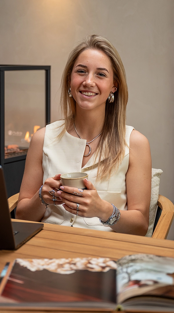 Interieurontwerpster Anouk glimlacht met een kopje thee tijdens een ontspannen moment aan tafel.