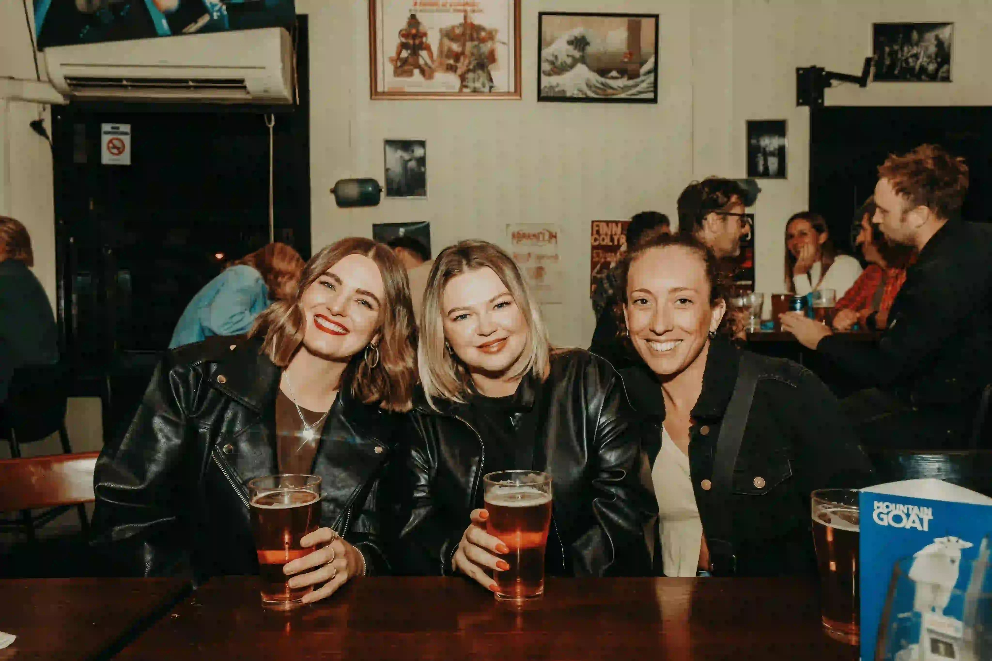 Three women sitting at a table with beers in front of them.