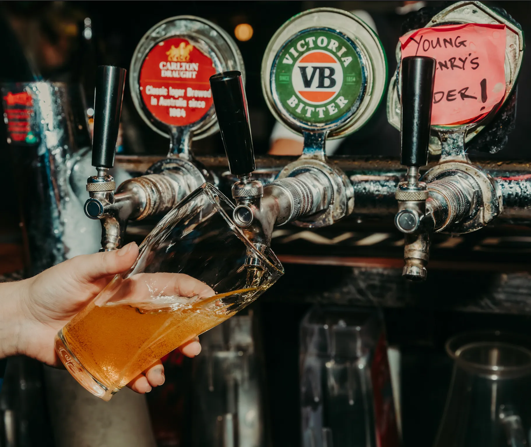 A person holding a glass of beer in front of a row of beer taps.