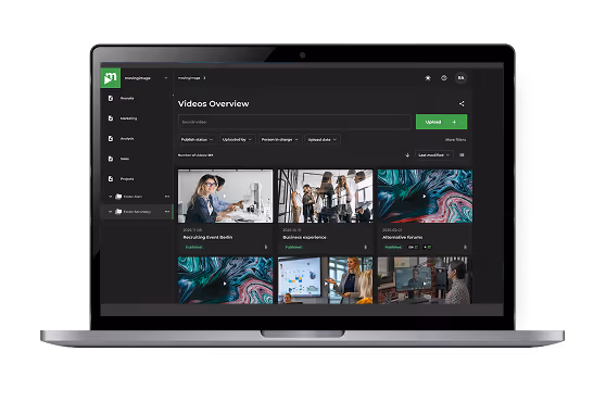 Laptop screen showing a video management dashboard with video thumbnails and upload options.