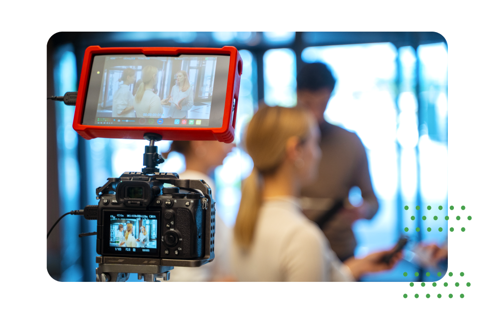 Professional camera with an external monitor recording an interview while people talk in the blurred background.