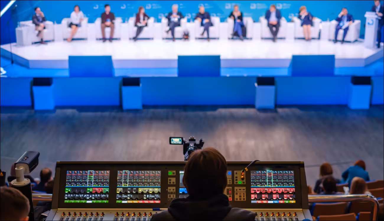 Camera and audio mixing desk filming a panel discussion with eleven speakers on a conference stage