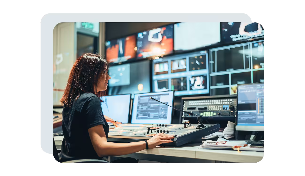 Technician operating a broadcast control desk in front of a wall of monitors during a live production