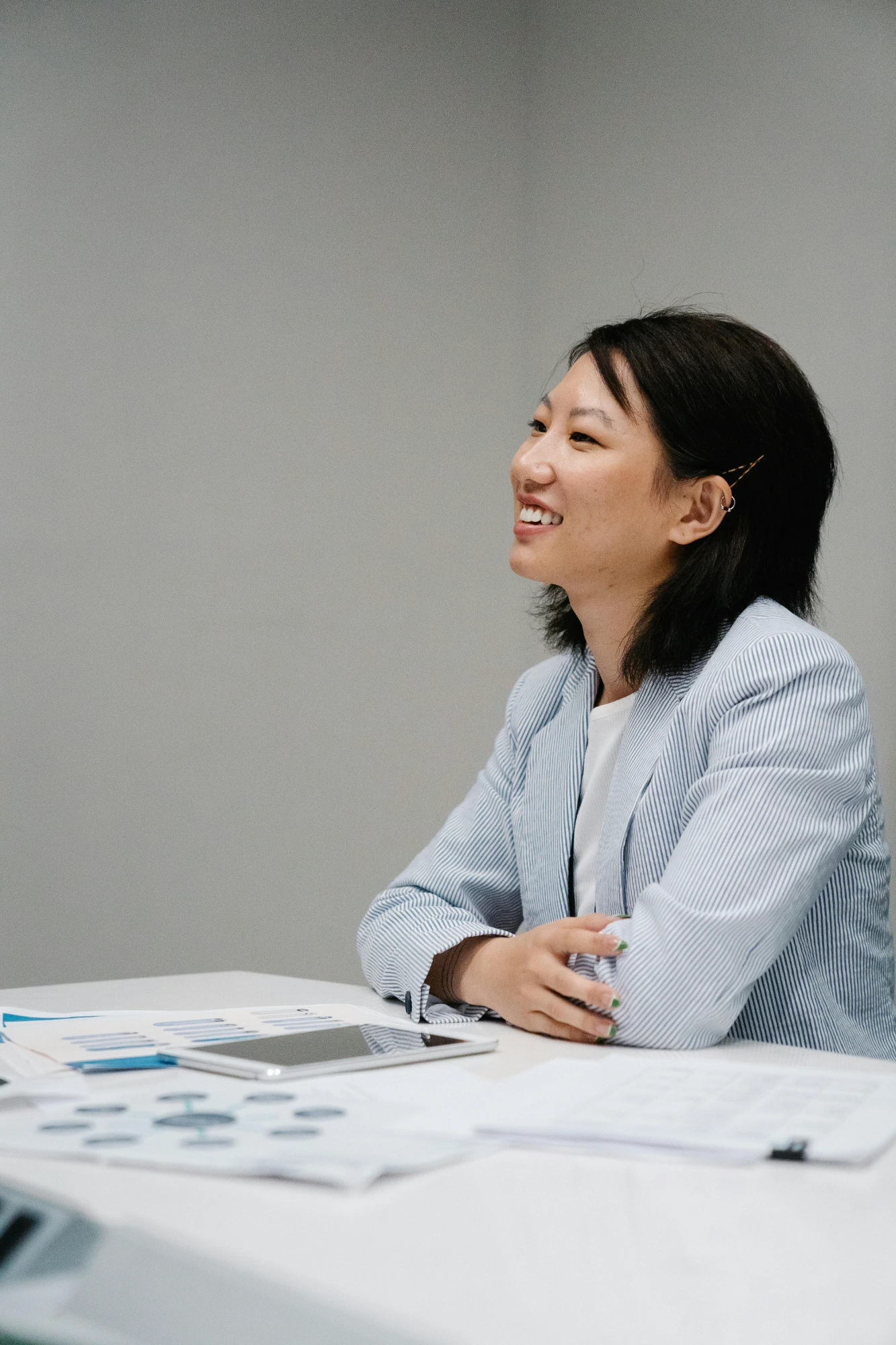 Smiling woman in a striped blazer sitting at a desk with documents and a tablet.