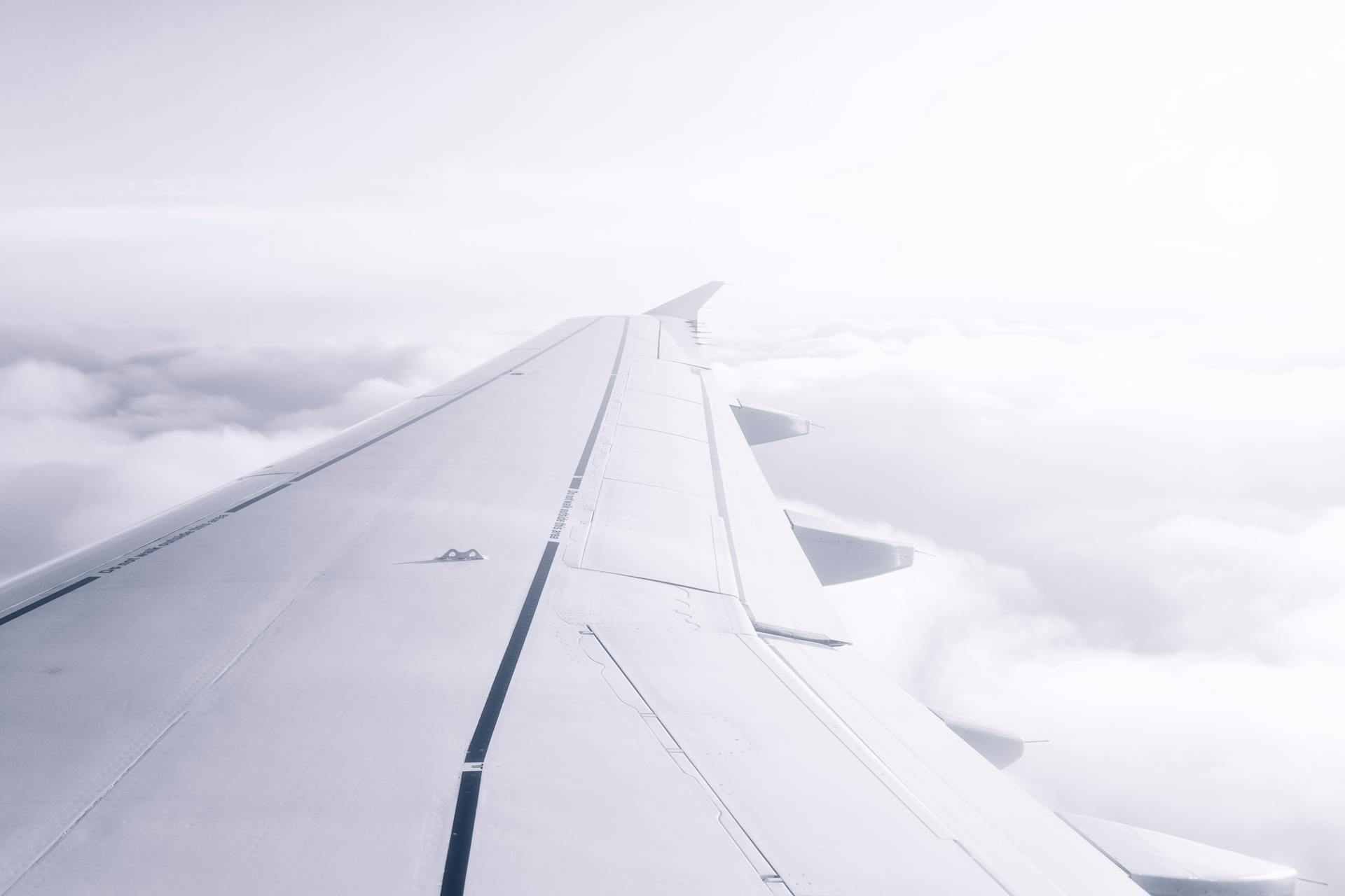 View of an airplane wing above fluffy white clouds under a bright sky.