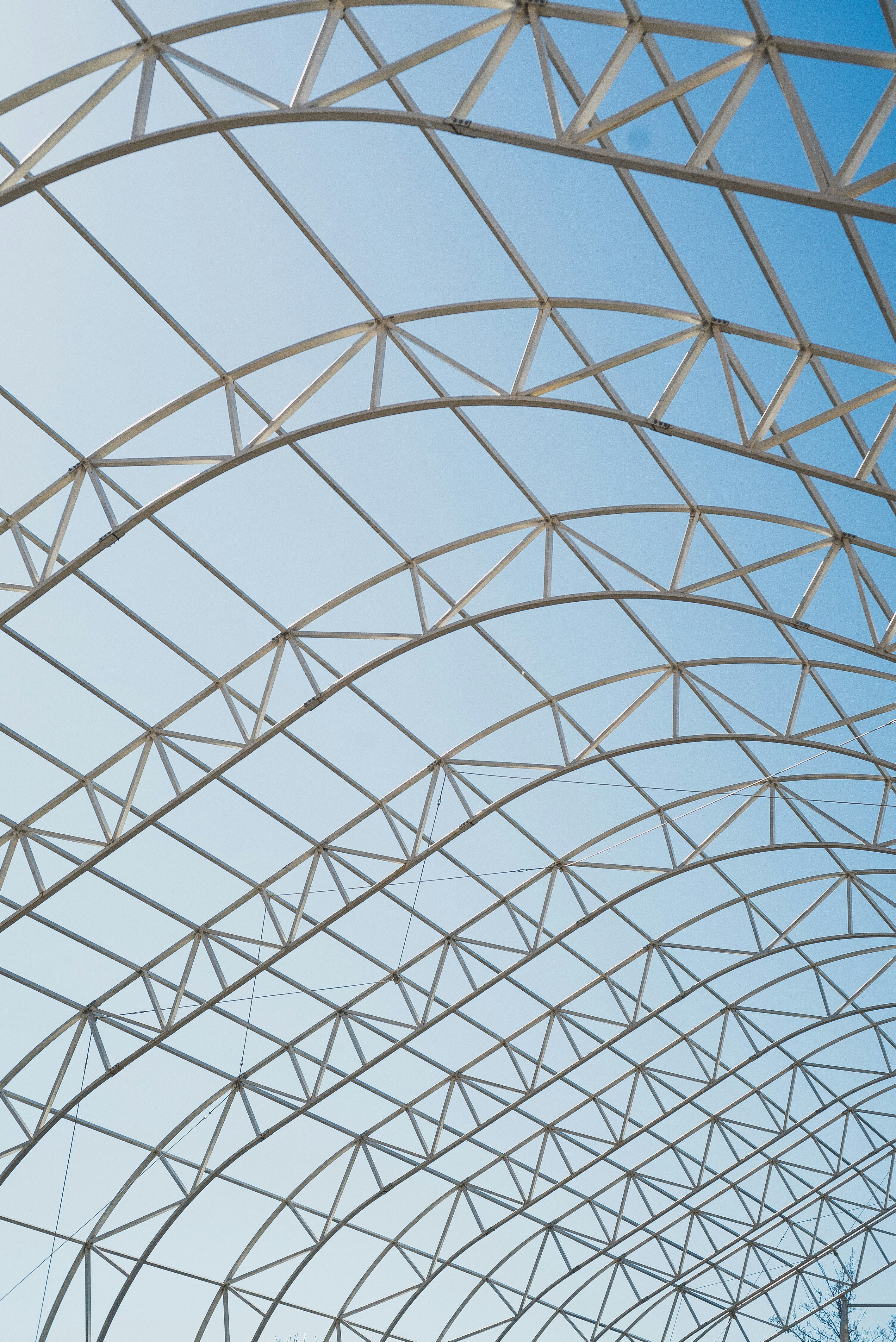 Curved metal framework structure against a clear blue sky.
