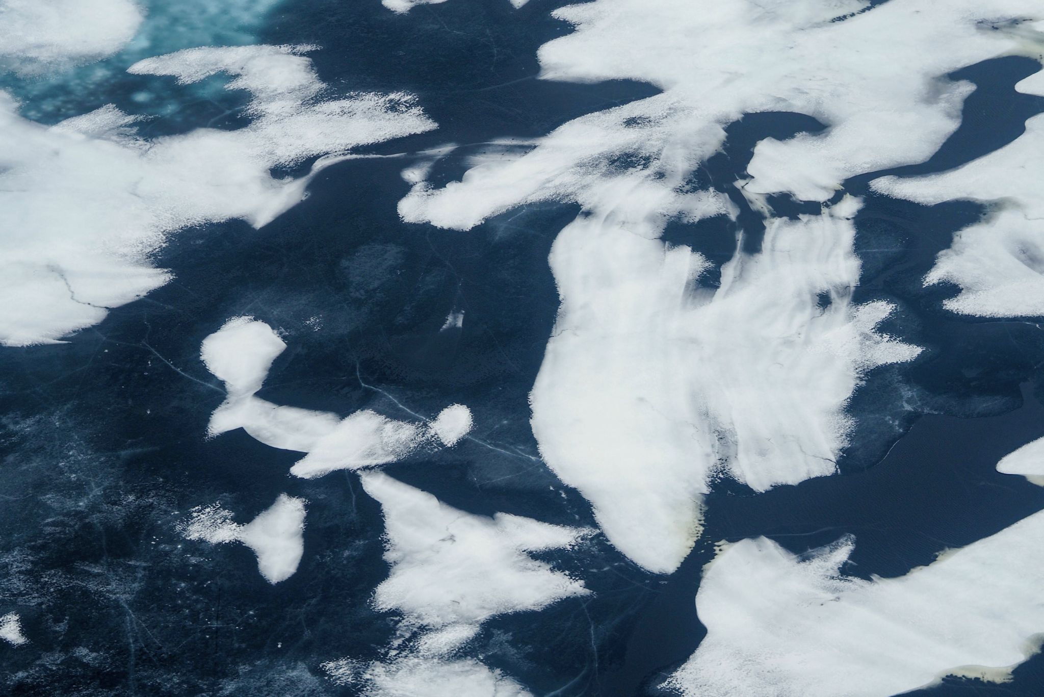Aerial view of fragmented sea ice floating on dark ocean water with visible cracks and textures.