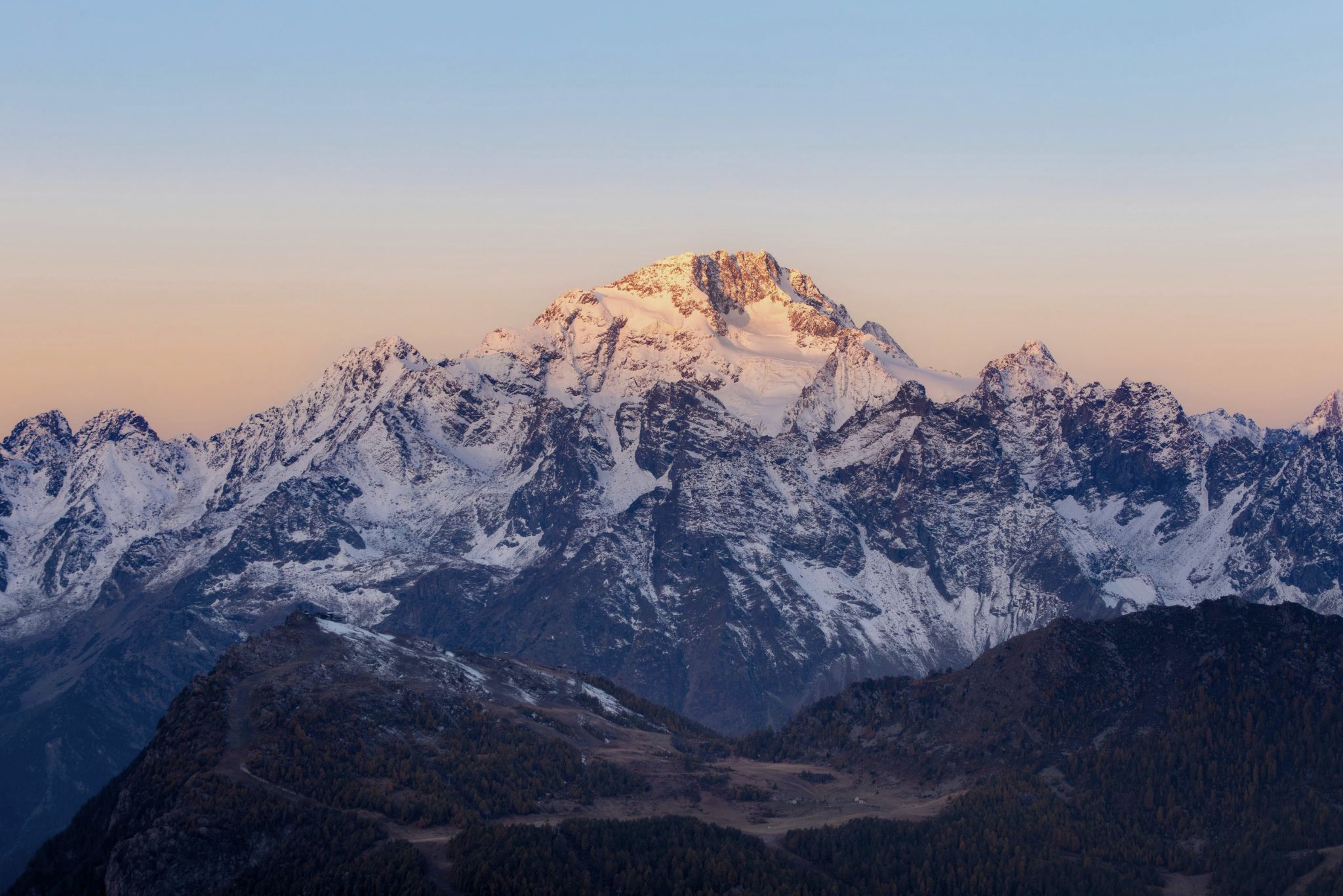 Snow-covered mountain peaks illuminated by soft sunset light under a clear sky.