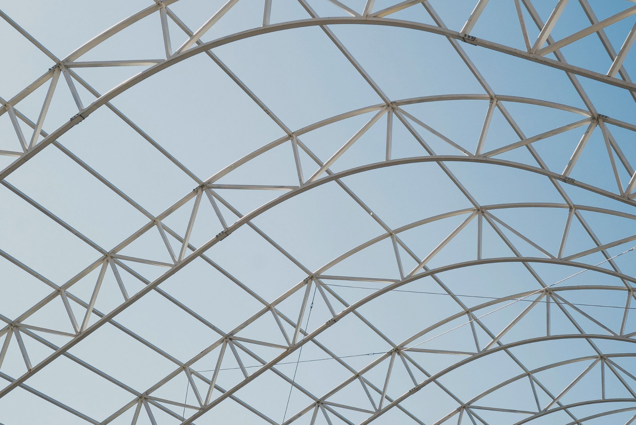 Curved metal truss framework against a clear blue sky.