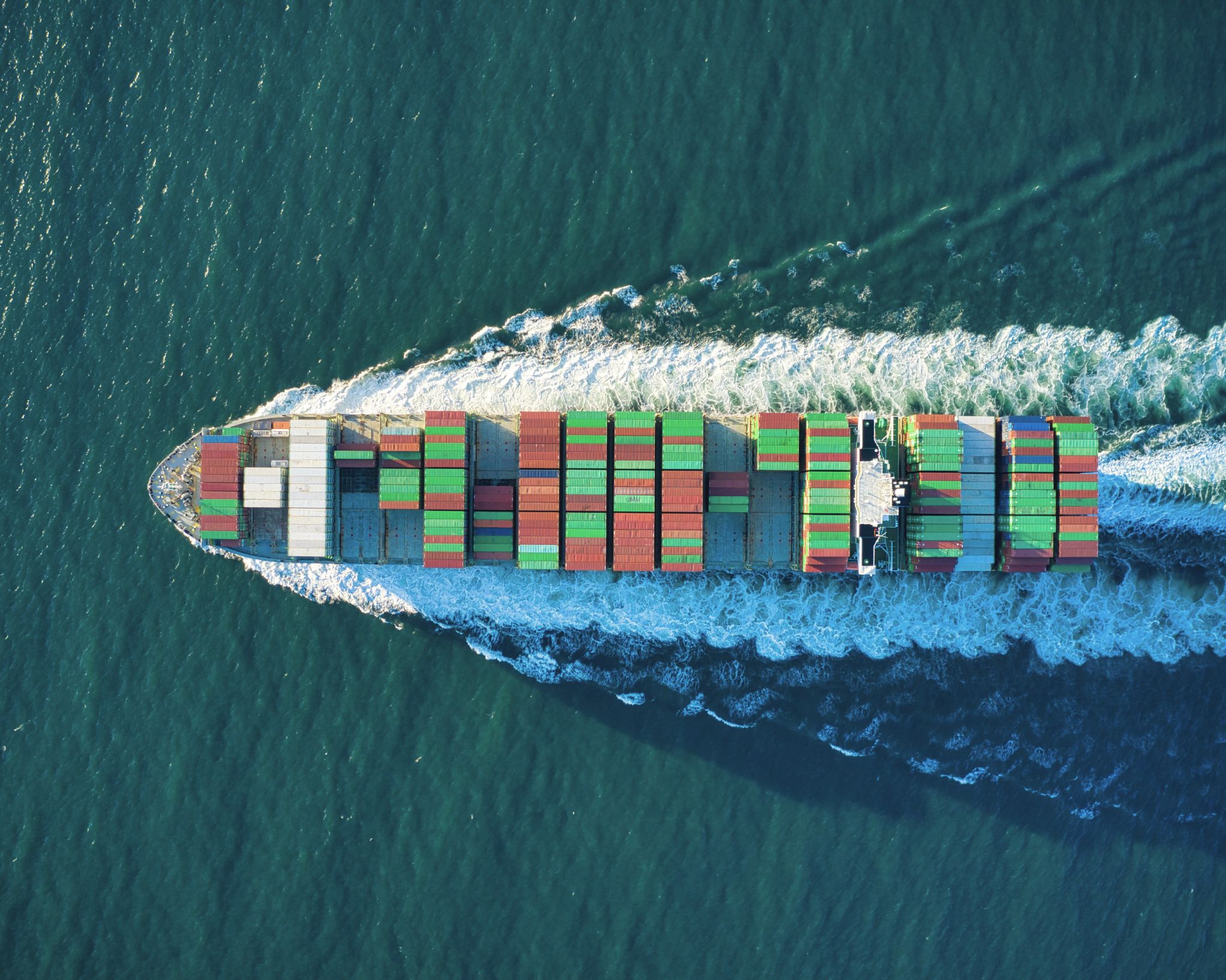 Aerial view of a container ship sailing through the ocean with colorful stacked shipping containers.