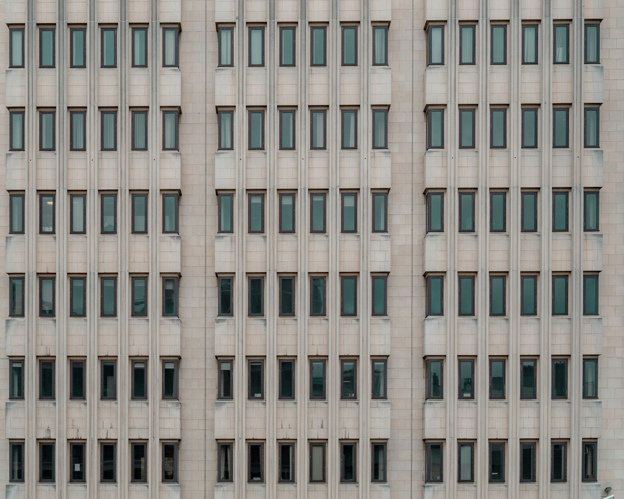 Facade of a building showing a repetitive grid pattern of narrow rectangular windows with beige stone panels.