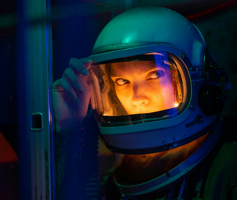 Dunkle Szenerie mit einer blonden Astronautin mit erleuchtetem Helm.