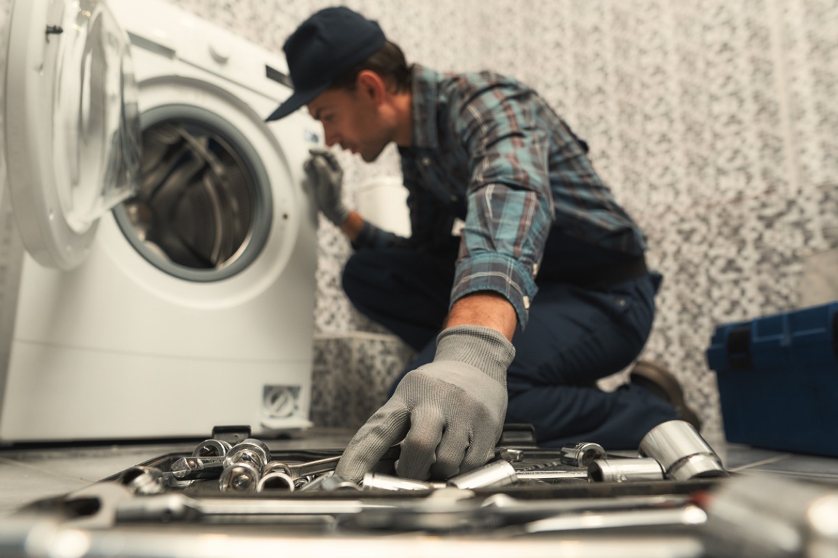 Technician repairing washing machine with tools spread on floor