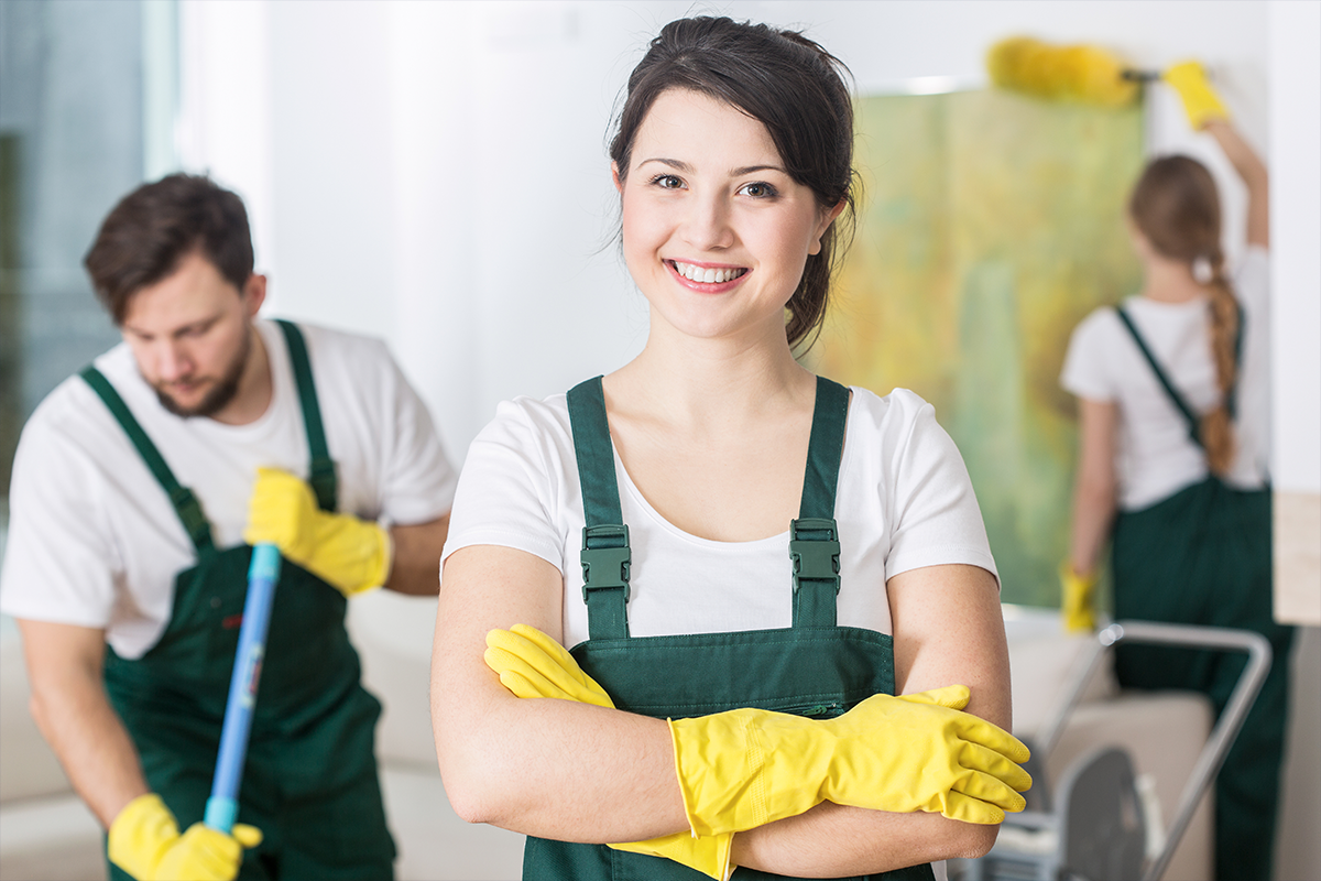 Smiling cleaning team in green uniforms and yellow gloves ready to work
