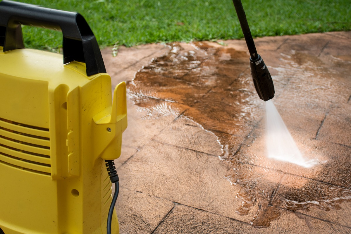 Yellow pressure washer cleaning dirty concrete patio or sidewalk surface