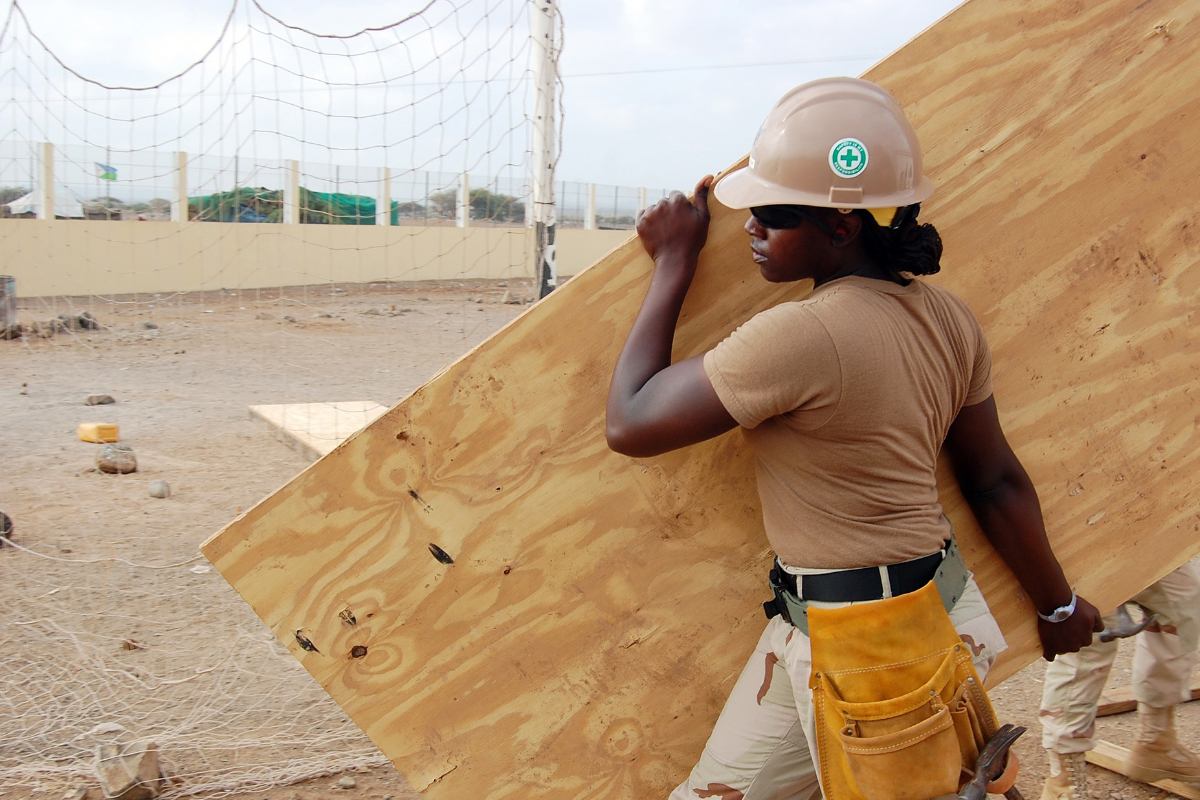 Construction worker carrying plywood sheet at outdoor site wearing safety helmet