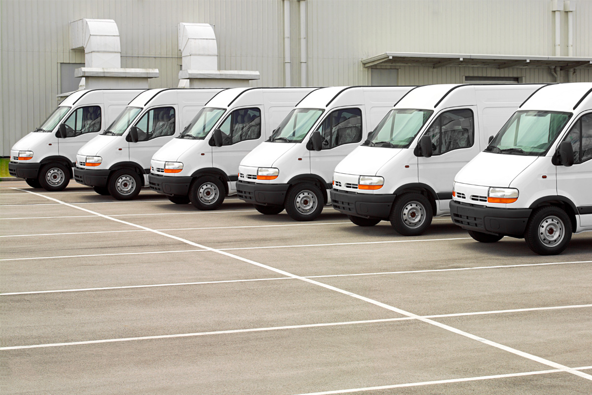 Several white delivery vans parked in a row in an industrial parking lot