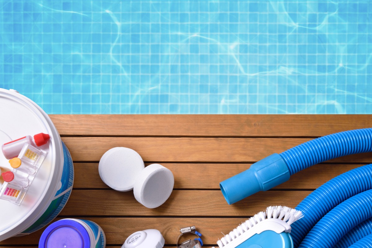 Swimming pool maintenance tools and cleaning supplies on wooden deck