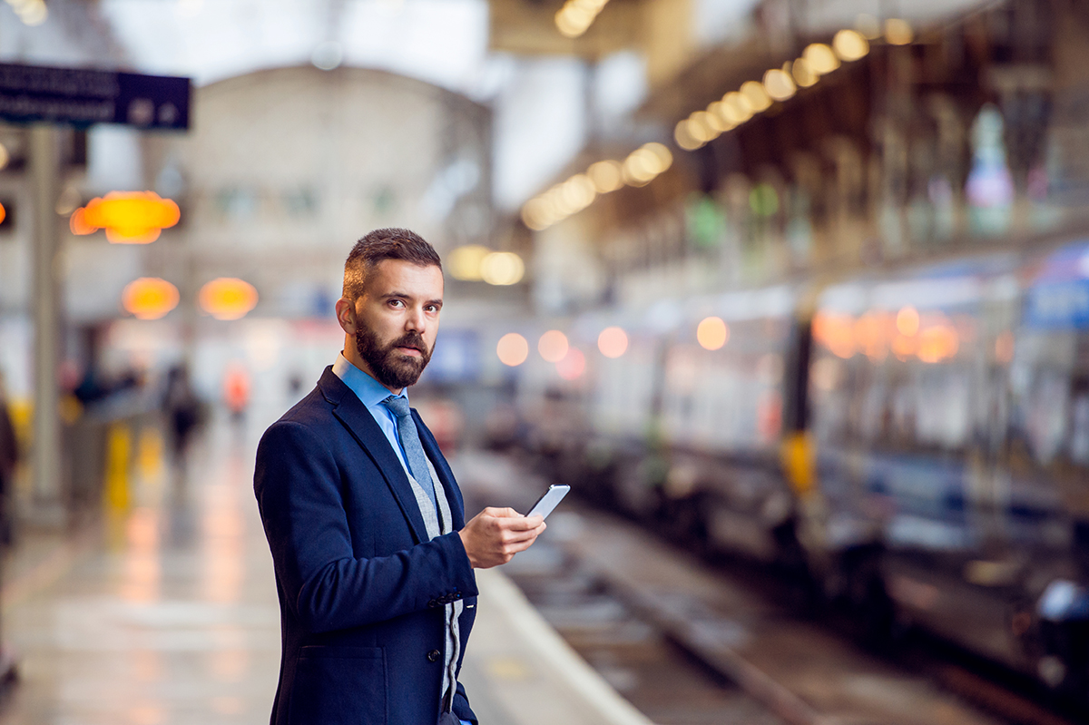 Businessman checking phone at train station platform with blurred background