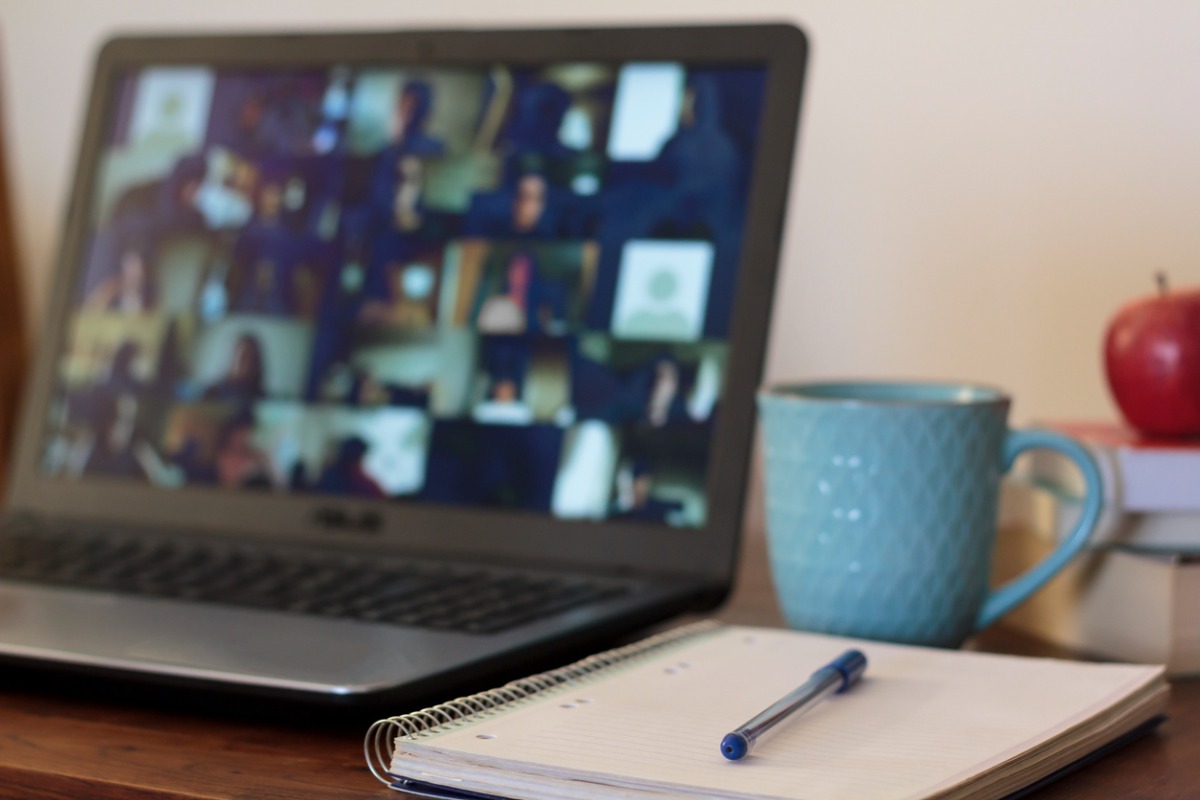 Laptop with video conference, notebook, blue mug, and red apple
