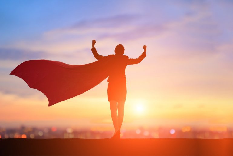 Silhouette of victorious person with cape standing against sunset skyline