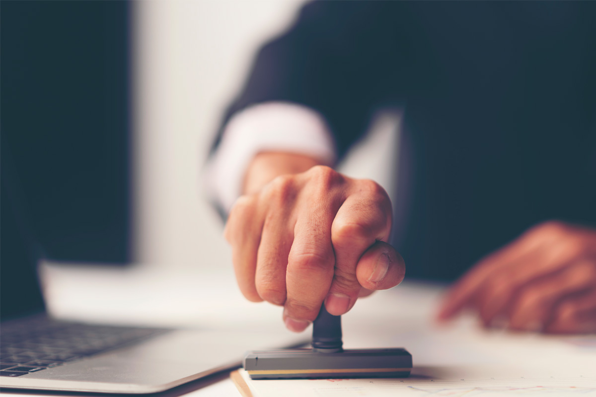 Hand pressing rubber stamp on desk next to laptop