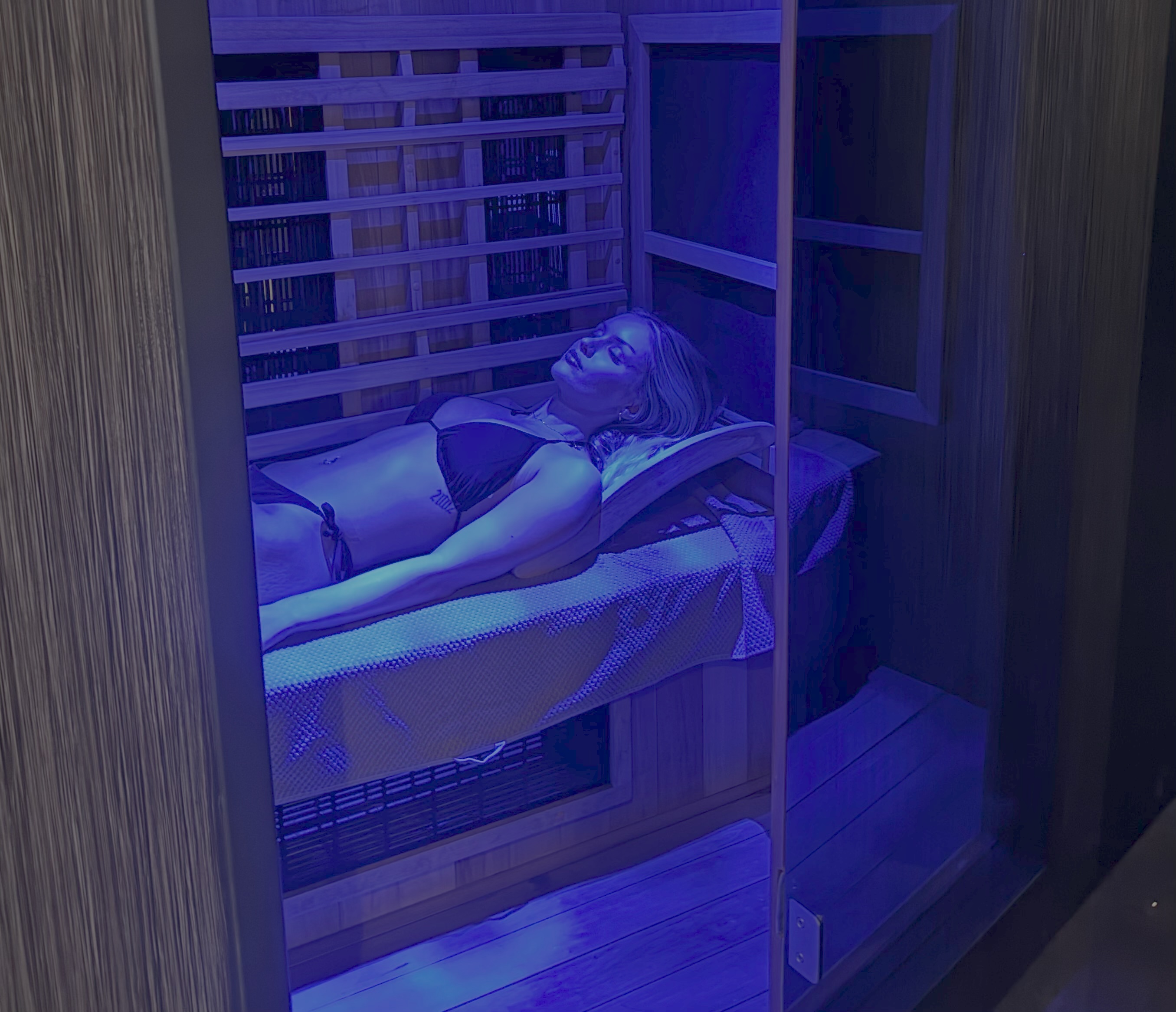 Woman lying down inside infrared sauna at ONE DZ Gym in Derby under blue light therapy