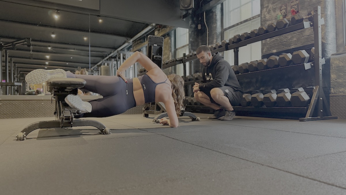 Female client performing glute-focused side plank with coach feedback at ONE|DZ Gym