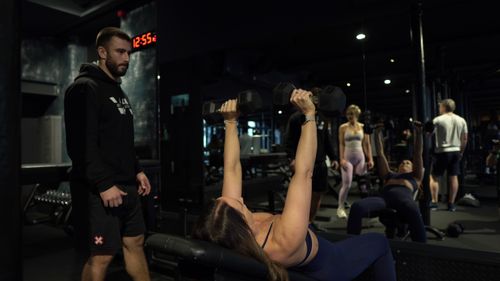 Woman coached through cable bicep curl during PT session at ONE|DZ Gym