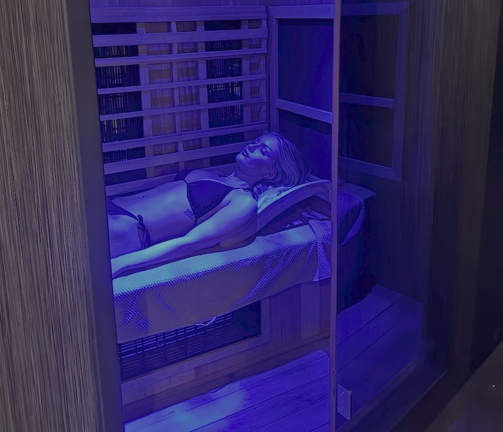 Woman lying down inside infrared sauna at ONE DZ Gym in Derby under blue light therapy
