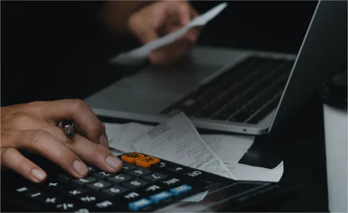 Person using a calculator in front of a laptop