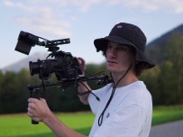 Молодий чоловік у чорному панамному капелюсі знімає відео професійною камерою на стабілізаторі на фоні природи та гір