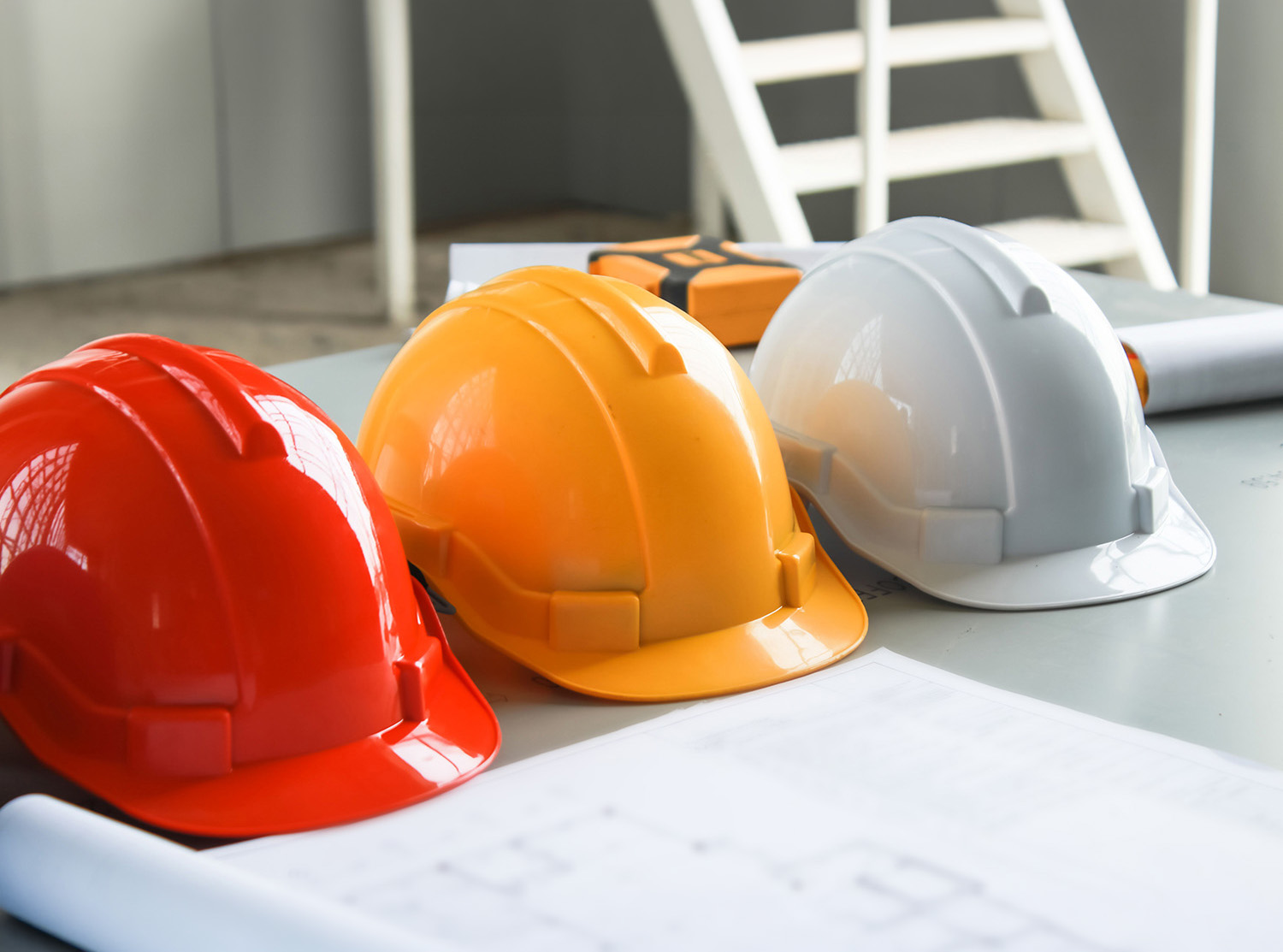Three construction hats line up in a row with blueprint