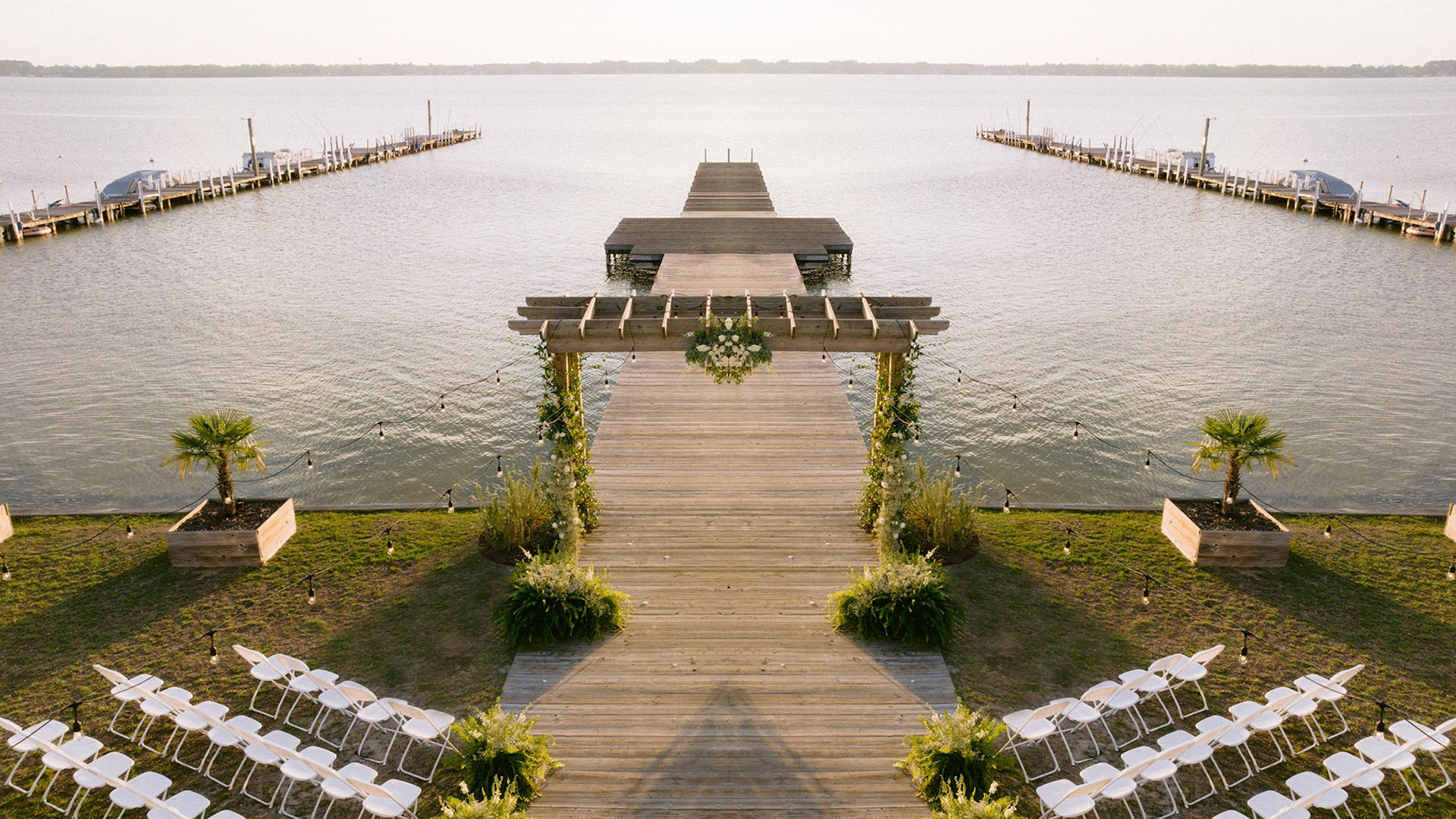 Lakeside wedding venue with wooden pier, floral arch, and white chairs