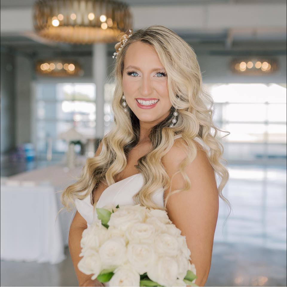 Bride in white dress smiling, holding white rose bouquet in elegant venue