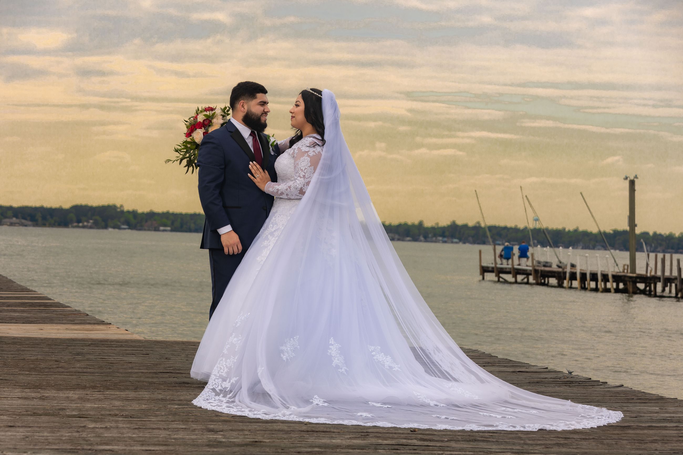 Wedding couple embracing on wooden pier with lake and sunset backdrop
