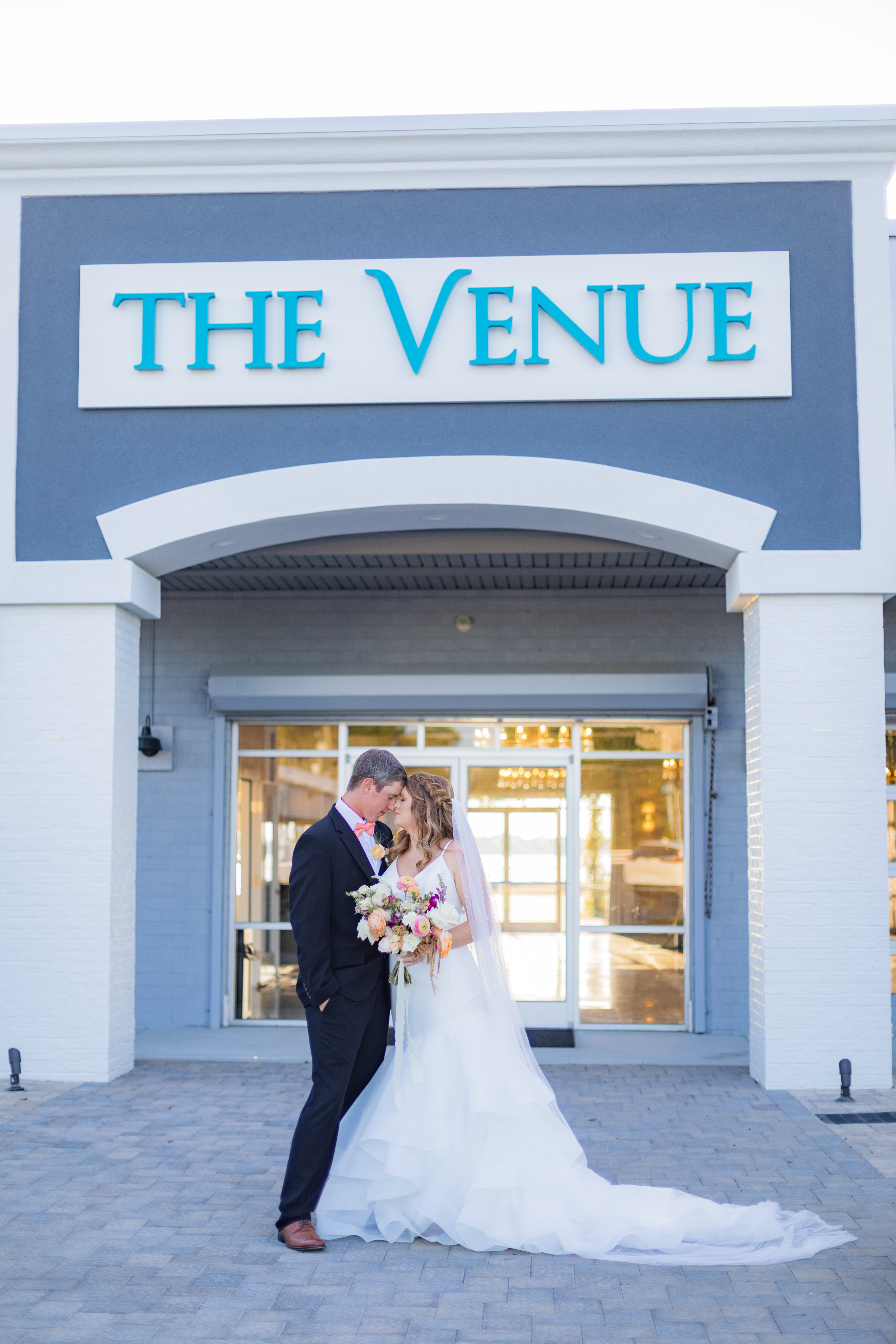 Wedding couple embracing in front of The Venue with blue and white sign