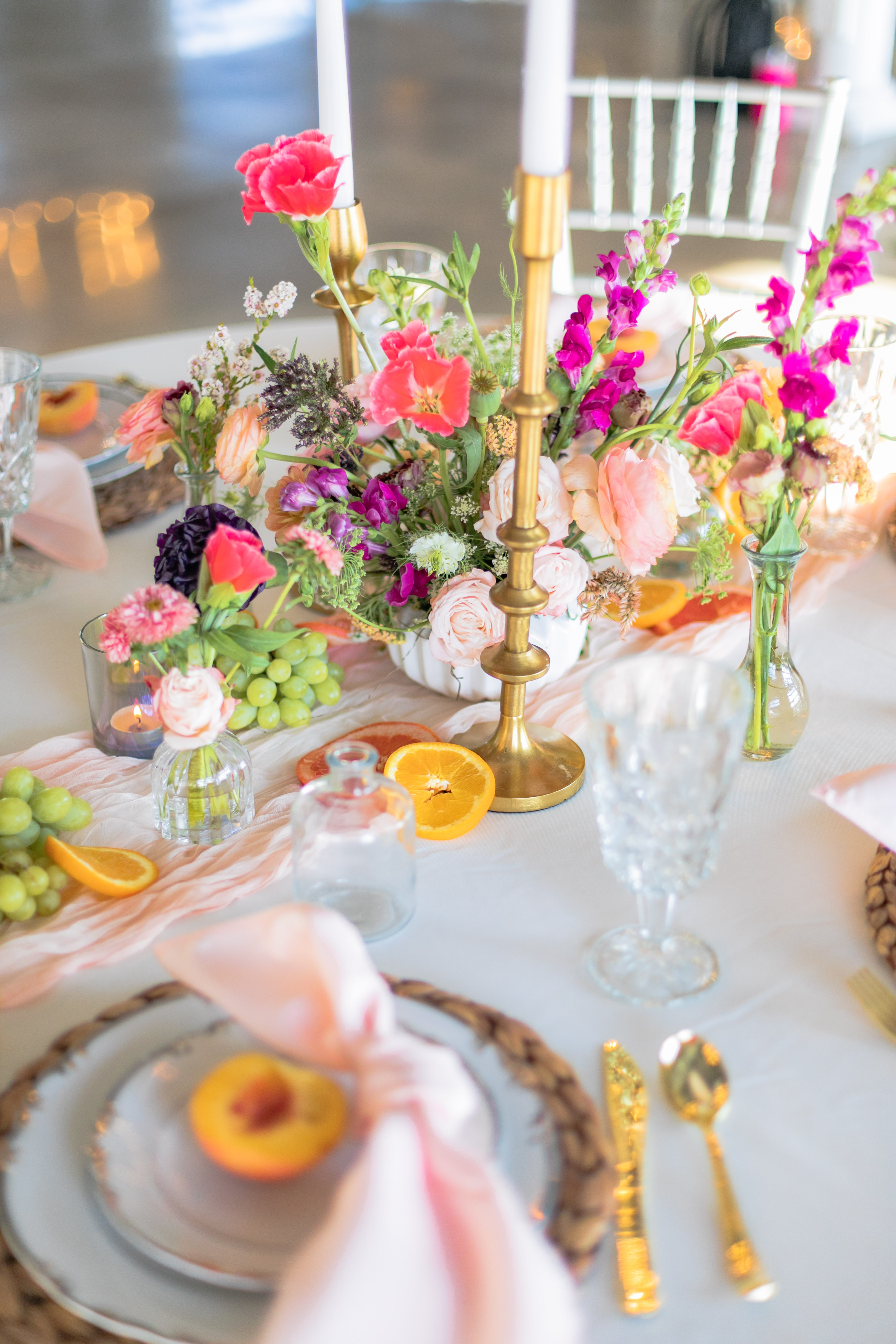 Colorful table setting with vibrant floral centerpiece, fruits, and golden candlestick